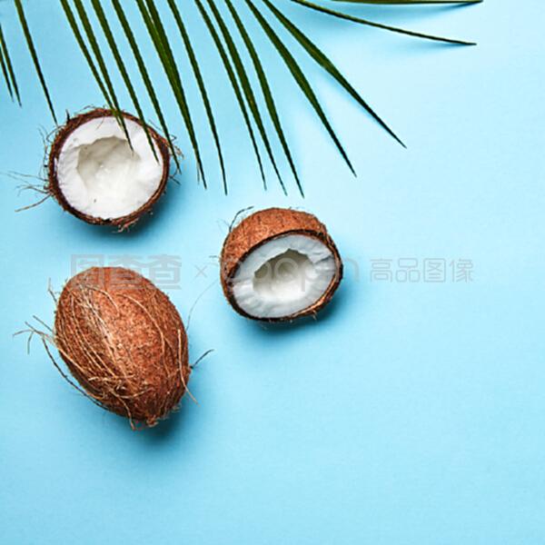 整個(gè)和一半的椰子,在藍(lán)色背景上的棕櫚葉和文本空間的副本。一個(gè)奇異的水果。扁平放。一個(gè)椰子和棕櫚綠葉在藍(lán)色背景上的副本空間。熱帶堅(jiān)果。扁平放。